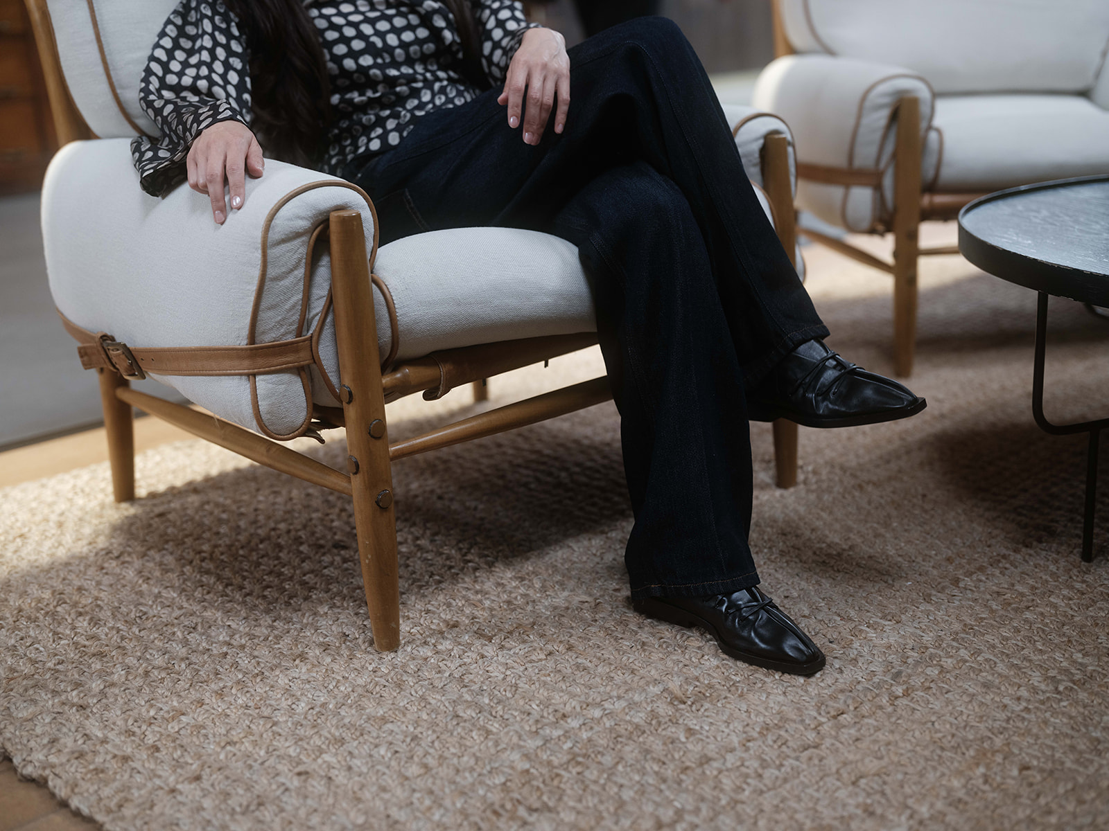 Bela Shehu seated in a light upholstered chair with crossed legs